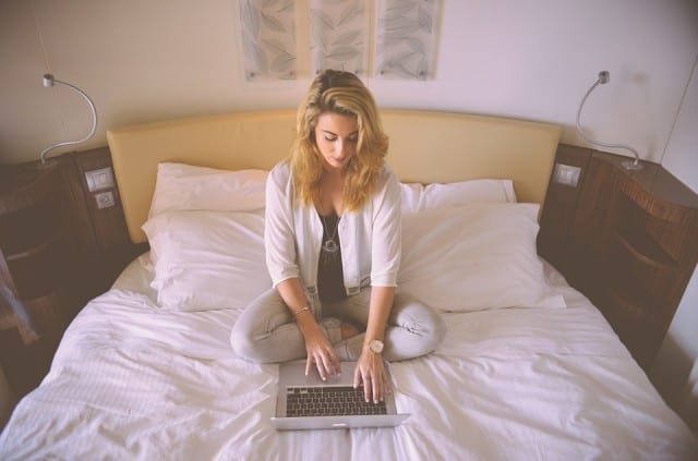 a woman sitting on a bed shopping on a laptop