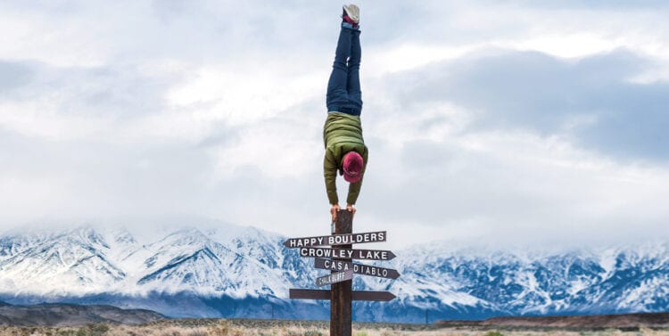 Man doing a handstand on a sign post wearing a Patagoinia jacket