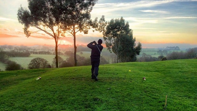 man teeing off at a golf course at sunrise